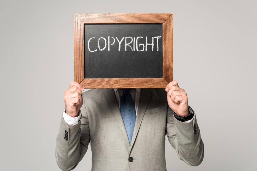 uomo d'affari volto oscuro con lavagna con iscrizione sul copyright isolato su grigio
 - Foto, immagini