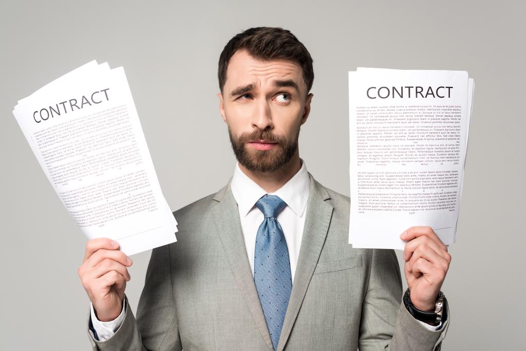 sceptische zakenman houdt contracten en kijkt weg geïsoleerd op grijs - Foto, afbeelding