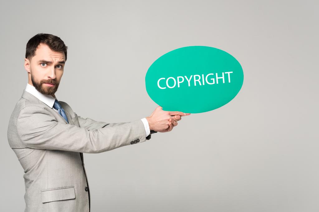 hombre de negocios serio sosteniendo burbuja de pensamiento con inscripción de derechos de autor aislado en gris
 - Foto, imagen