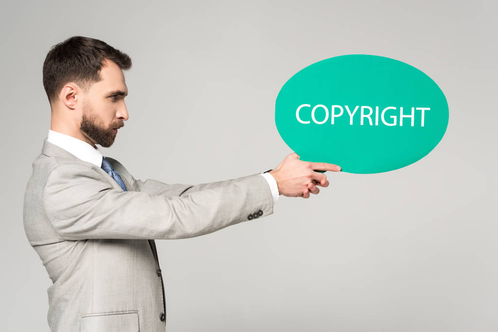 Seitenansicht eines selbstbewussten Geschäftsmannes mit Sprechblase und Worturheberrecht isoliert auf grau - Foto, Bild