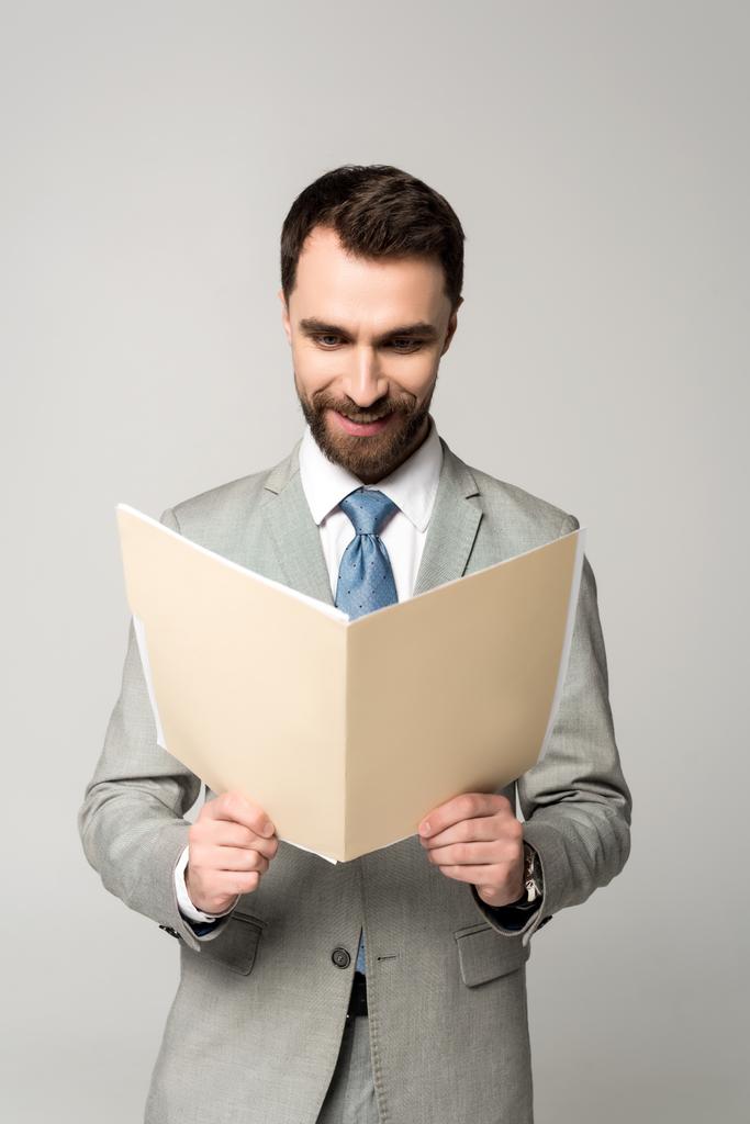 sonriente hombre de negocios leyendo documentos en la carpeta de papel aislado en gris
 - Foto, Imagen