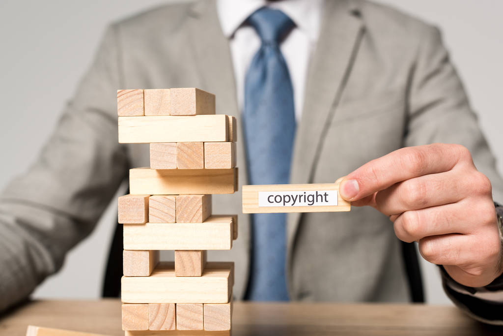 Teilansicht eines Geschäftsmannes mit Holzblock mit Urheberrechtsbeschriftung isoliert auf grau - Foto, Bild