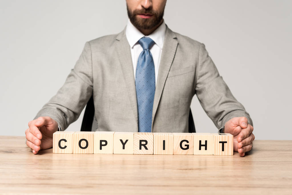 cropped view of businessman sitting at desk near wooden cubes with word copyright isolated on grey - Photo, Image