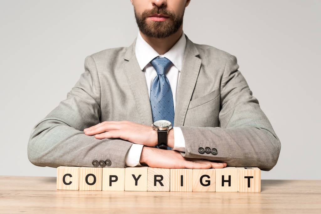 частковий вид на бізнесмена, що сидить за столом біля дерев'яних кубиків зі словом авторське право ізольовано на сірому
 - Фото, зображення
