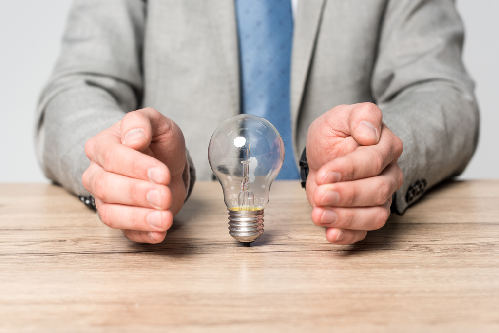 partial view of businessman showing protection gesture near light bulb isolated on grey - Photo, Image