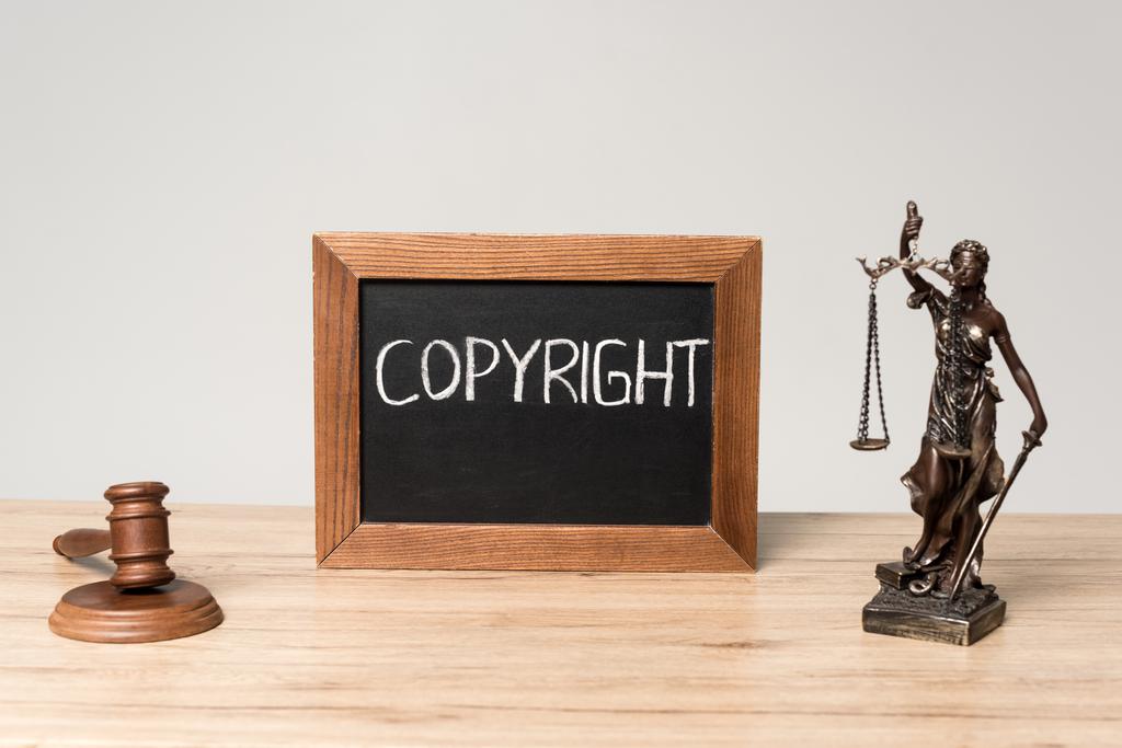 krijtbord met woord copyright, het standbeeld en hamer op houten bureau geïsoleerd op grijs - Foto, afbeelding