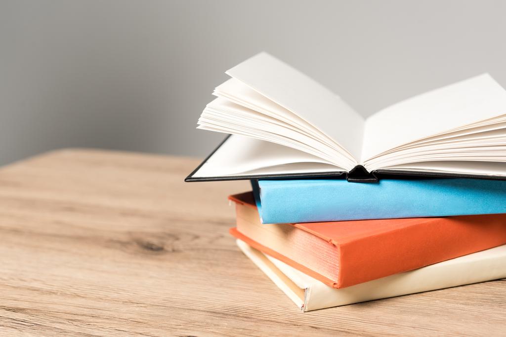 pila de libros y cuaderno abierto en blanco sobre escritorio de madera sobre fondo gris
 - Foto, Imagen
