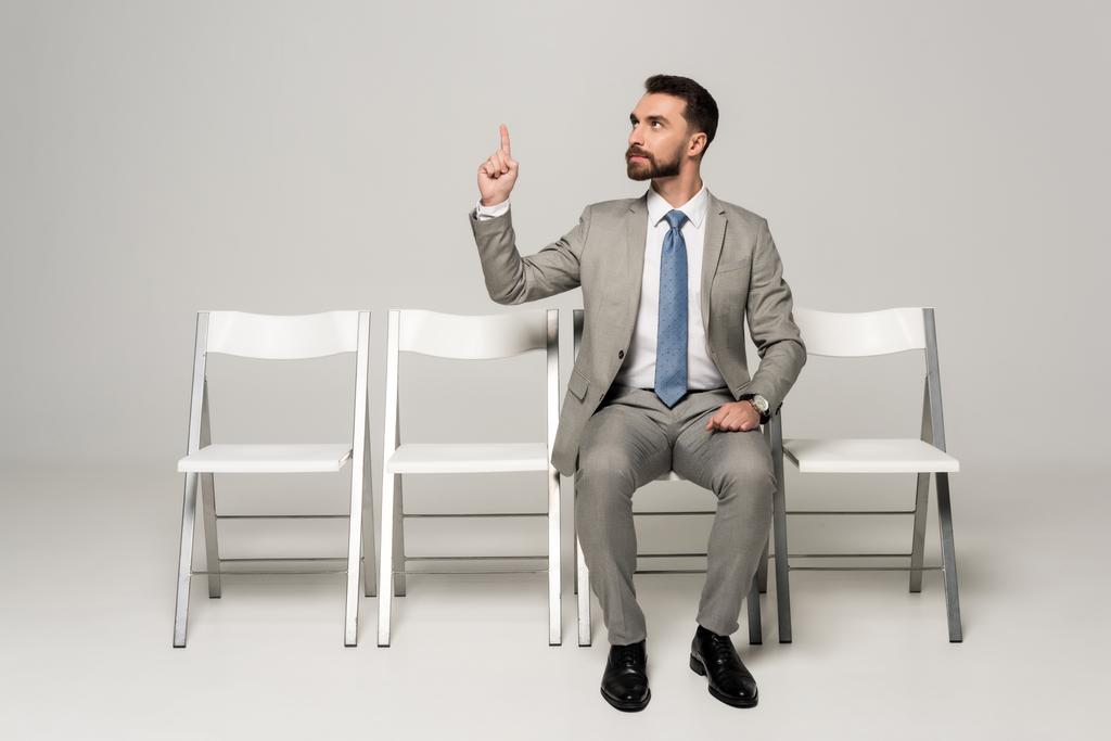 уверенный бизнесмен сидит на стуле и показывает жест идеи на сером фоне
 - Фото, изображение