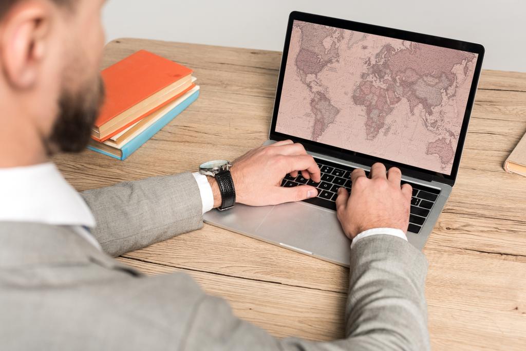 vista recortada del hombre de negocios utilizando el ordenador portátil con el mapa del mundo en la pantalla aislada en gris
 - Foto, imagen