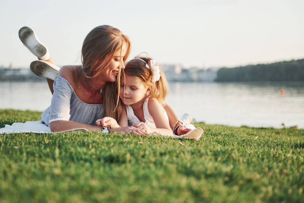 Atrakcyjne szczęśliwy młoda matka leżąca ze swoją uroczą córką na trawie w parku - Zdjęcie, obraz