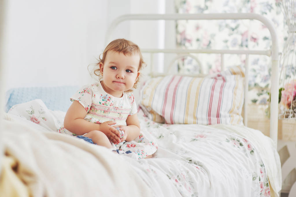 Gyerekkori koncepció. baba lány aranyos ruhát ül az ágyban játszik játékokat az otthoni. Fehér szüret gyermekszoba. - Fotó, kép