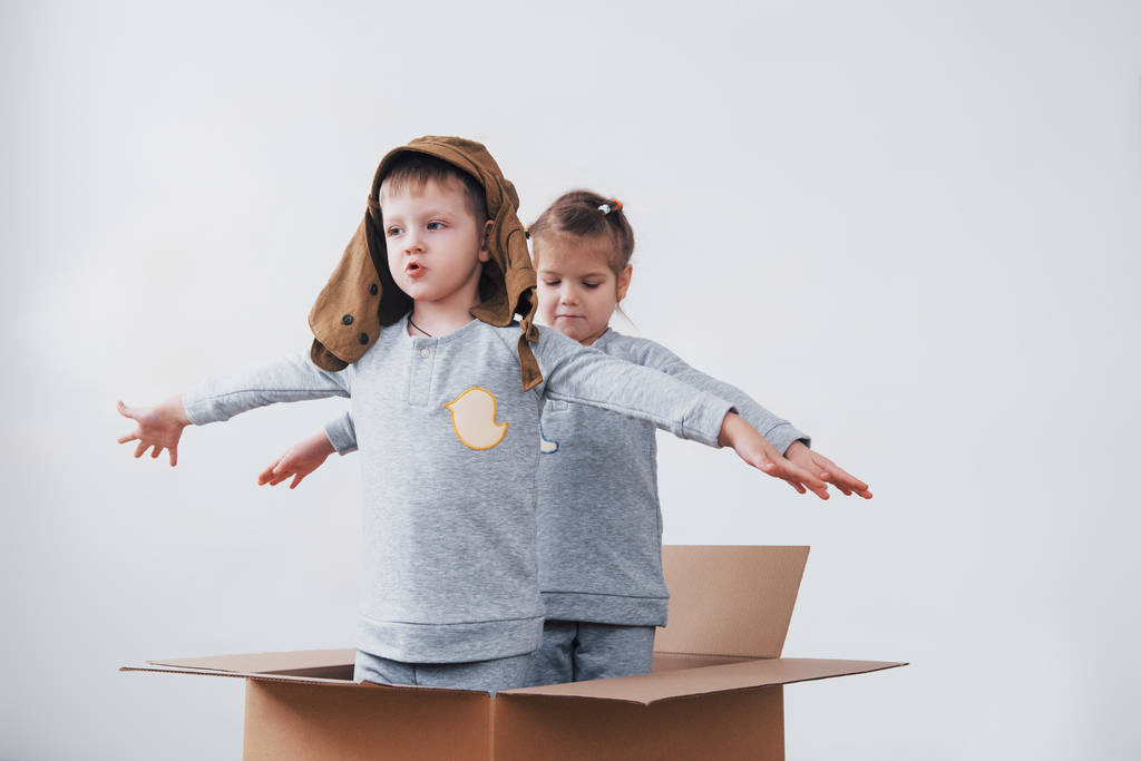 Playful childhood. Little boy having fun with cardboard box. Boy pretending to be pilot. Little boy and girl having fun at home. - Photo, Image