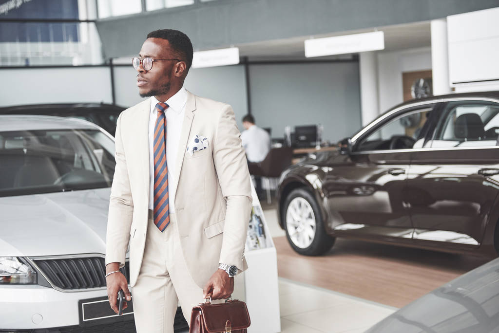 Jeune homme d'affaires noir sur fond de salon automobile. Concept de vente et location de voiture
. - Photo, image