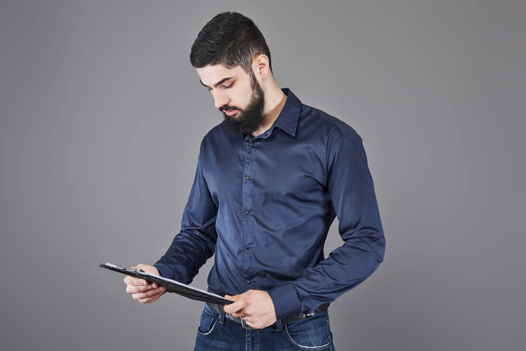 Concentré jeune homme d'affaires attrayant dans la planification chemise bleue et l'écriture dans le presse-papiers
. - Photo, image