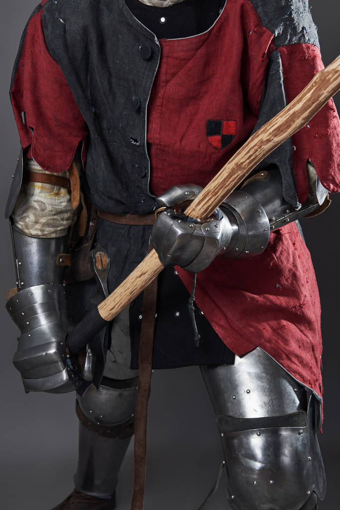 Středověký rytíř na šedém pozadí. Portrét brutálního špinavého obličeje válečníka s kroužkovou zbrojí červené a černé oblečení a válečnou sekerou. - Fotografie, Obrázek