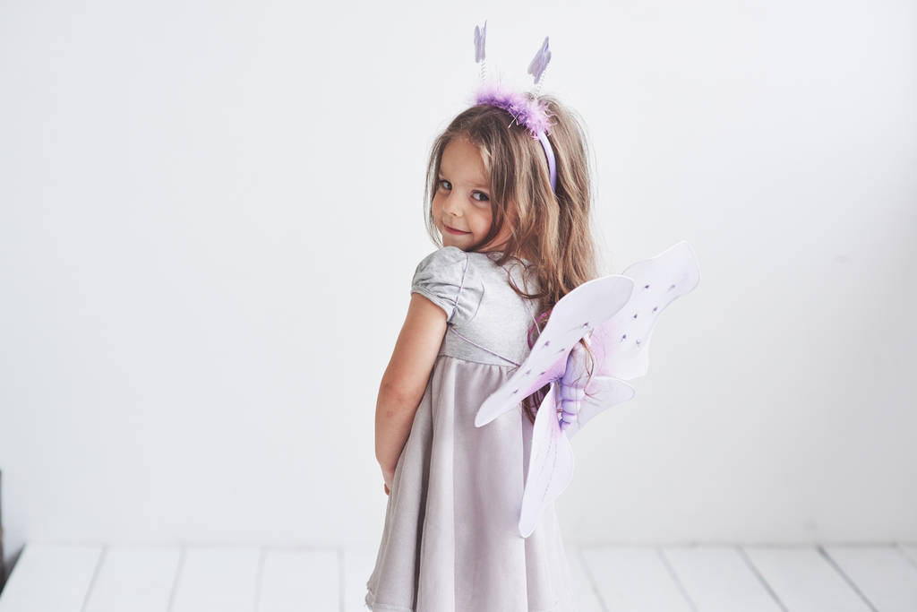 Shy look. Lovely little girl in the fairy costume standing in room with white background. - Photo, Image