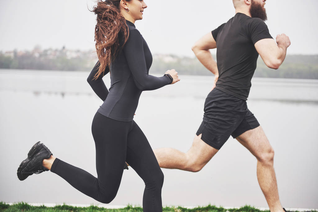 Couple jogging and running outdoors in park near the water. Young bearded man and woman exercising together in morning. - Photo, Image