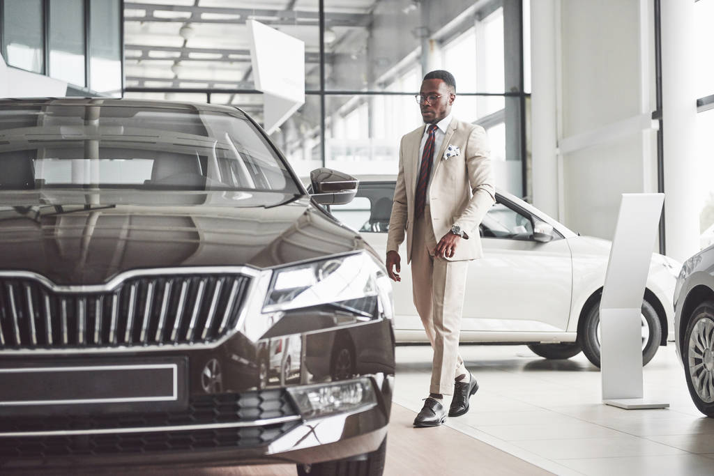 Fiatal fekete üzletember, autószalon háttérrel. Autóeladás és bérleti díj koncepció. Gazdag afro-amerikai férfi. - Fotó, kép