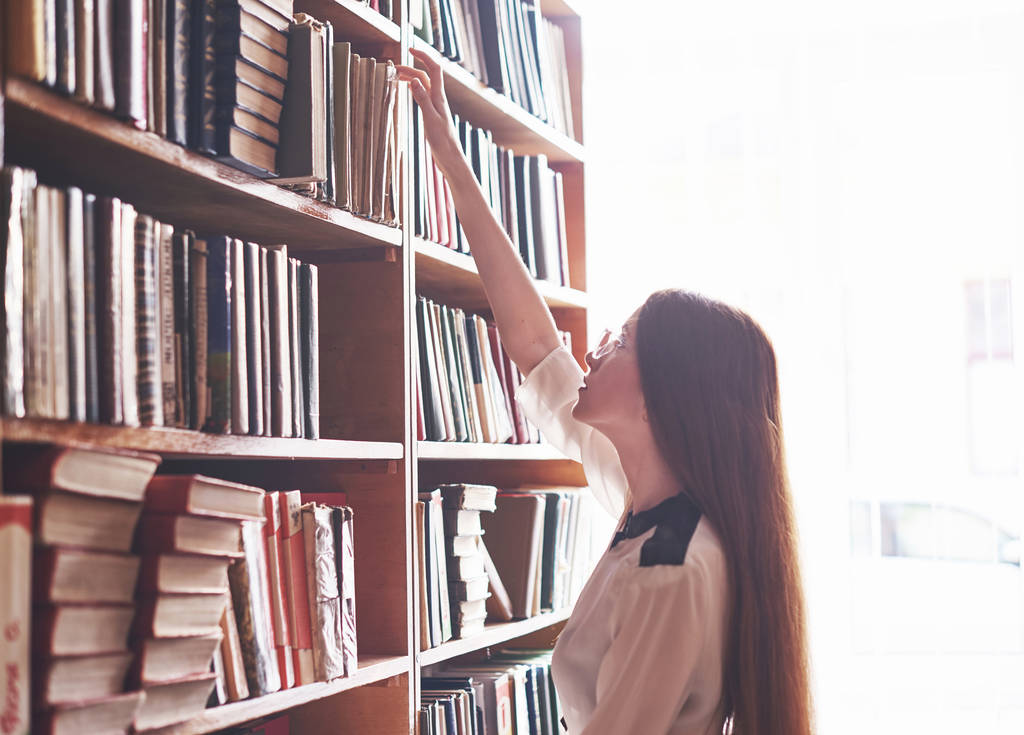 Une jeune étudiante cherche le bon livre sur les étagères de l'ancienne bibliothèque universitaire
. - Photo, image