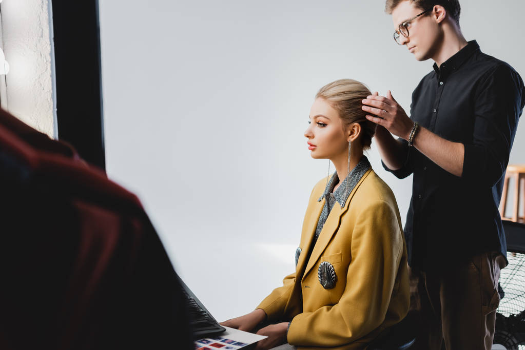 Zijaanzicht van hairstylist doen kapsel naar stijlvol model op backstage   - Foto, afbeelding