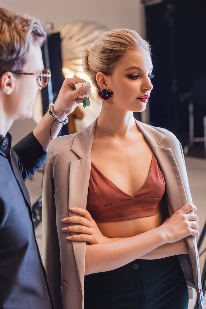 bijgesneden weergave van stylist kiezen oorbellen voor stijlvol model op backstage  - Foto, afbeelding