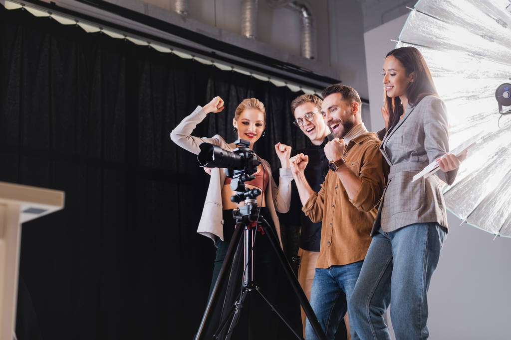 low angle view of smiling photographer, model, stylist and producer looking at digital camera and showing yes gesture on backstage  - Photo, Image
