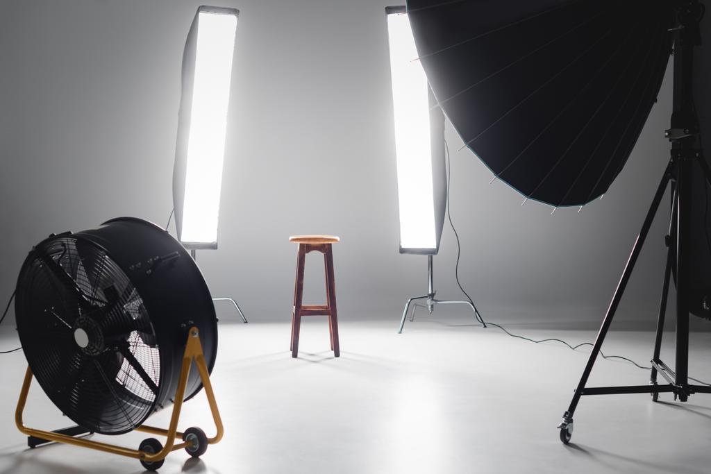digital camera, fan, reflector, wooden stool and lights on backstage in photo studio - Photo, Image