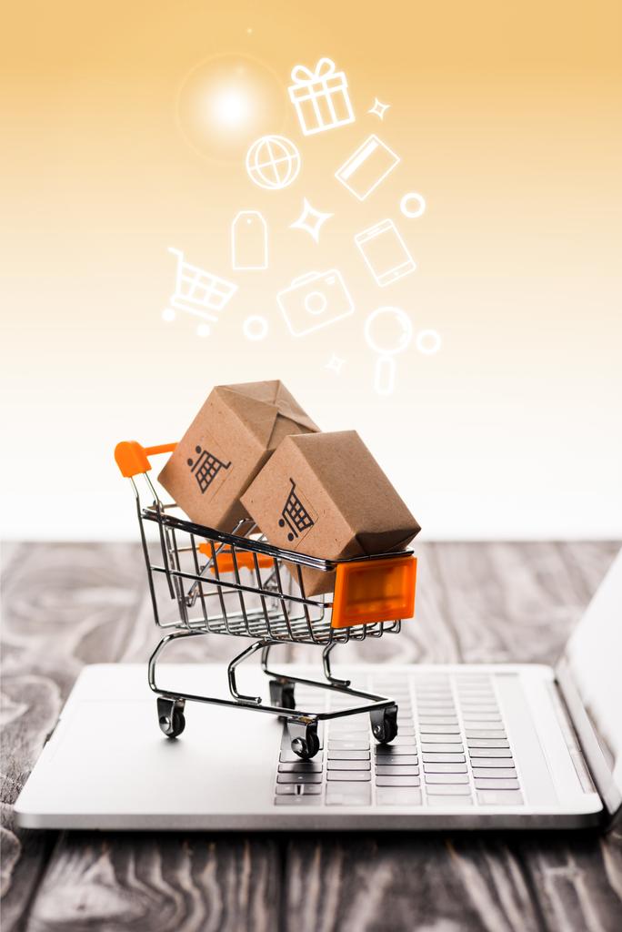 selektivní zaměření nákupního košíku hraček s malými kartonovými krabicemi na klávesnici notebooku u ilustrace na oranžové, e-commerce koncept - Fotografie, Obrázek