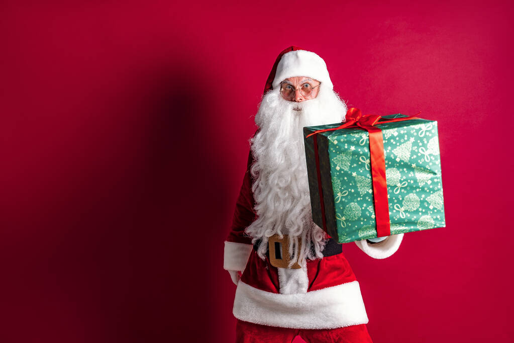 Foto de tipo Santa Claus dando regalo de Navidad y mirando a la cámara
 - Foto, Imagen