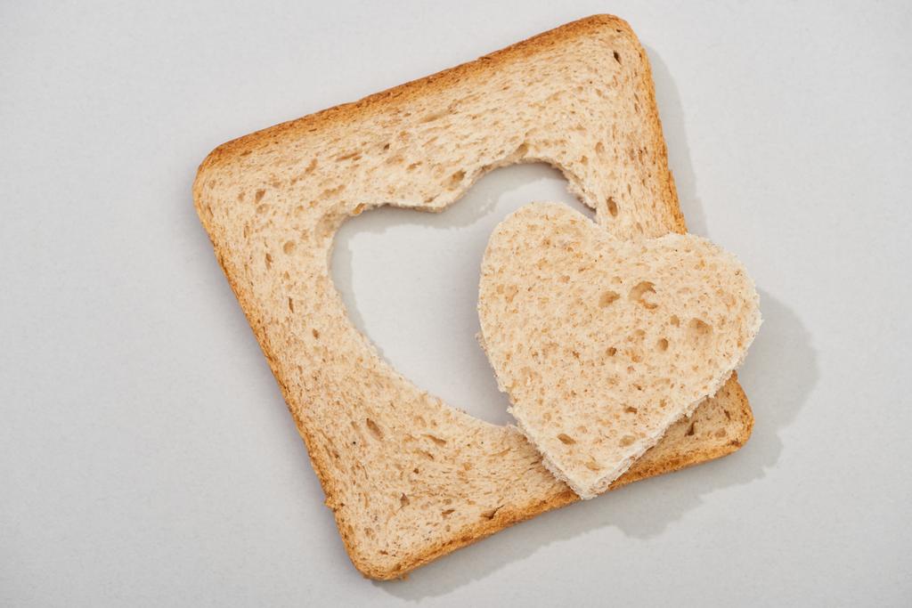 Gri arka planda oyulmuş bir kalple bir dilim ekmeğin en üst görüntüsü - Fotoğraf, Görsel