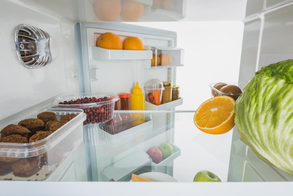 Vers fruit, koteletten en kool in de koelkast met open deur geïsoleerd op wit - Foto, afbeelding