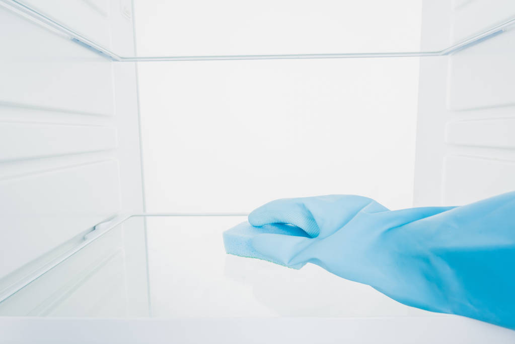 Gewassen weergave van de vrouw in rubber handschoen schoonmaken koelkast met spons op witte achtergrond - Foto, afbeelding