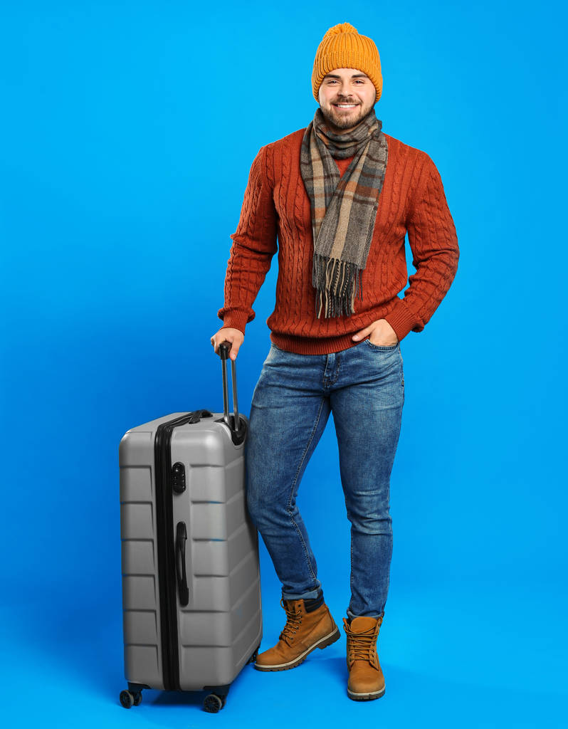 青い背景にスーツケースを着た暖かい服の若者。冬休み - 写真・画像