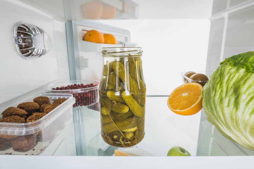 Jar of pickles with cabbage, fruits and cutlets in refrigerator with open door isolated on white - Photo, Image