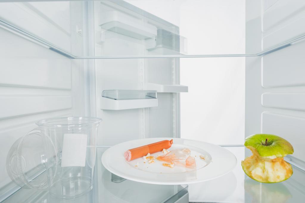 Lemez törmelékkel, harapott alma és műanyag pohár hűtőszekrényben nyitott ajtóval elszigetelt fehér - Fotó, kép