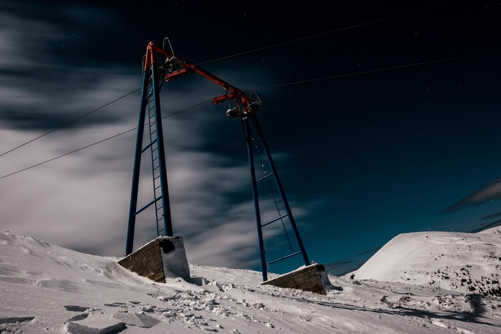vista panorámica del ascensor de góndola en la montaña cubierta de nieve contra el cielo oscuro con nubes blancas
 - Foto, Imagen