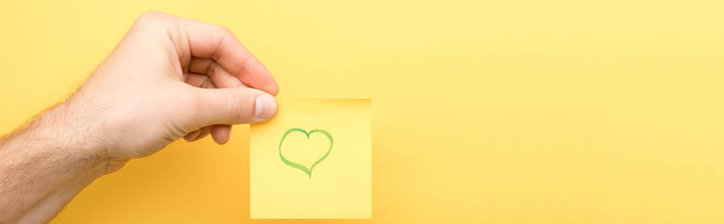 panoramic shot of man holding sticky note with heart on yellow background  - Photo, Image