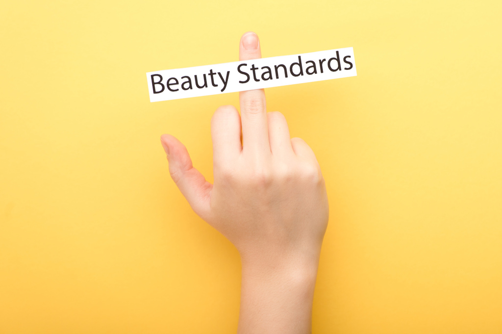 Orta parmak ve kartı sarı arka planda güzellik standartlarıyla gösteren bir kadın görüntüsü.  - Fotoğraf, Görsel
