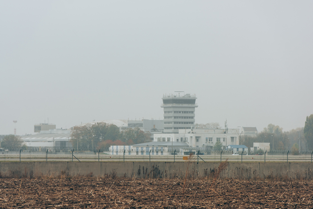 Aeródromo con pista de aterrizaje y edificios aeroportuarios con cielo nublado al fondo
 - Foto, Imagen