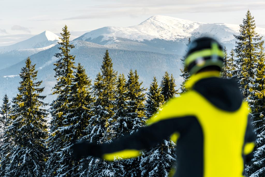 Selektiver Fokus des weißen Schnees auf grüne Tannen in der Nähe des Sportlers im Helm  - Foto, Bild