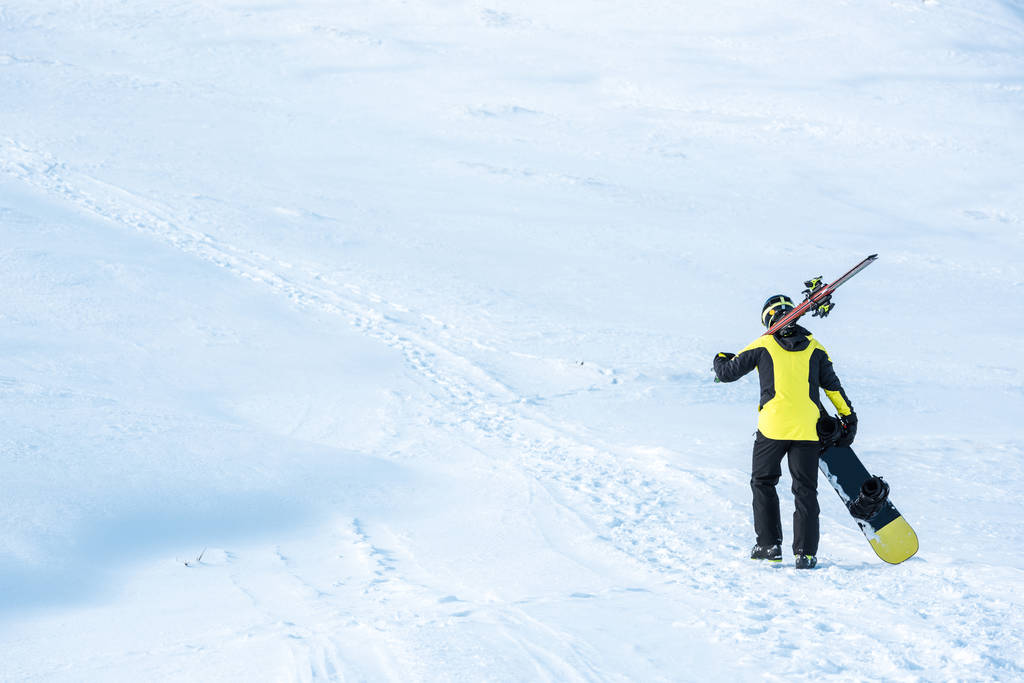 vue arrière du skieur en casque marchant avec des bâtons sur la neige blanche dans les montagnes
  - Photo, image