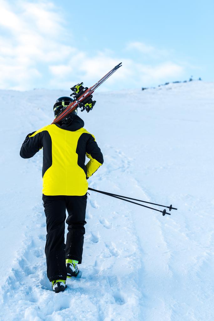 вид ззаду лижника в шоломі, що йде з лижними паличками на снігу
  - Фото, зображення