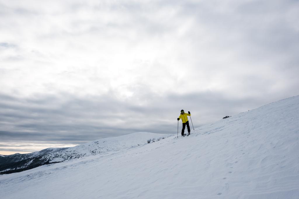 narciarz w kasku stojący z kijami narciarskimi na stoku zimą  - Zdjęcie, obraz