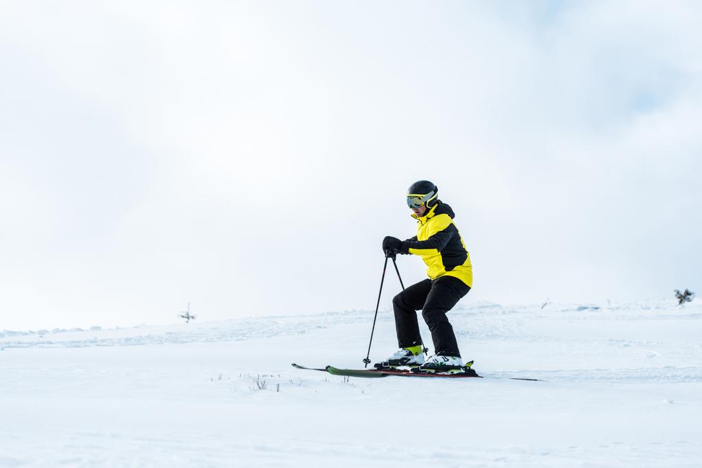 αθλητής στο κράνος κρατώντας μπαστούνια και σκι στην πλαγιά με χιόνι - Φωτογραφία, εικόνα
