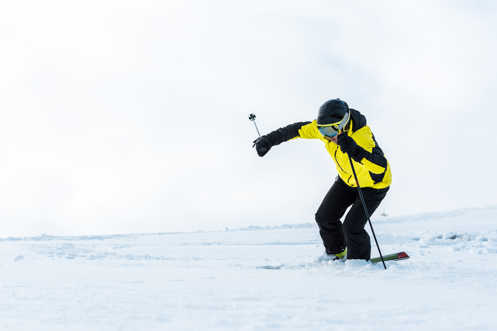 Sportler in Schutzbrille hält Stöcke in der Hand und fährt auf schneebedeckter Piste - Foto, Bild