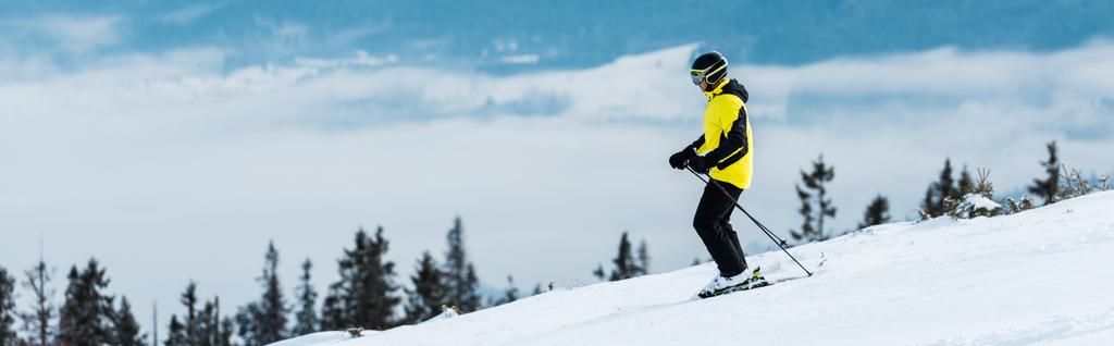 panoramatický záběr sportovce v helmě lyžování na svahu u hor  - Fotografie, Obrázek