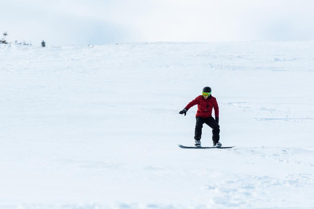 snowboarder en casco y guantes montados en pendiente con nieve blanca afuera
  - Foto, Imagen