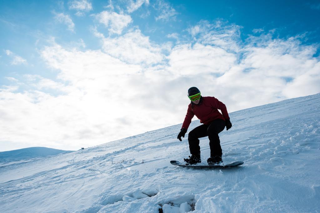 atletische snowboarder rijden op helling tegen blauwe lucht in de winter  - Foto, afbeelding