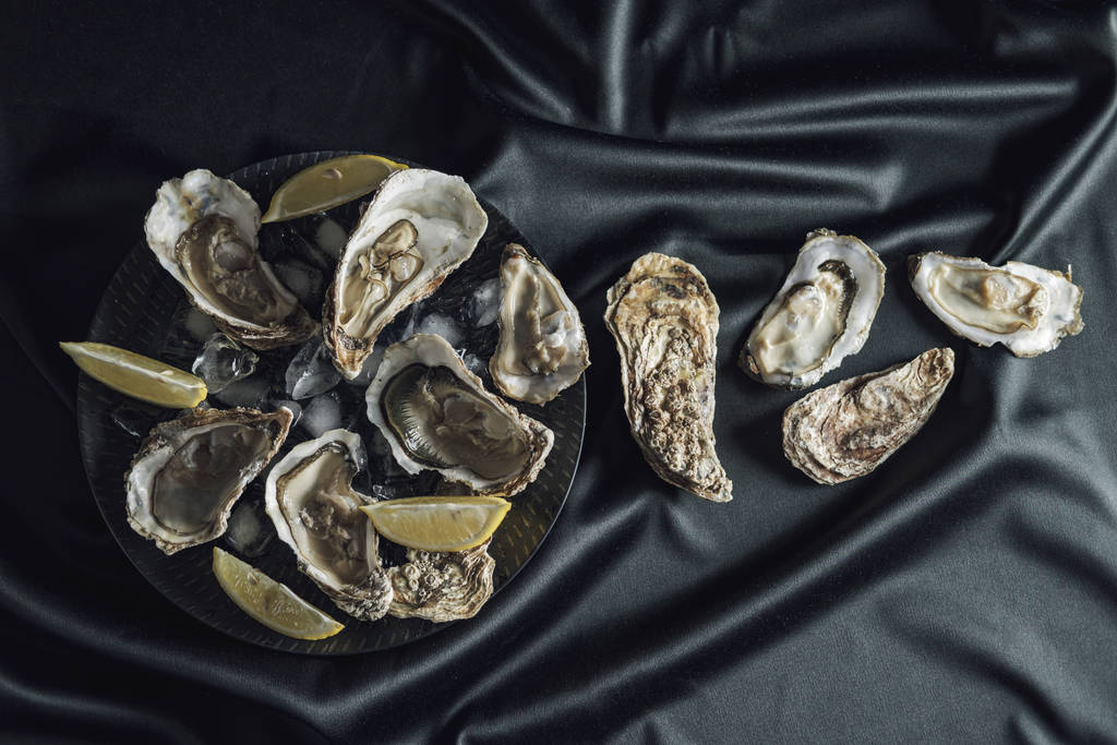 Open oesters met citroen in een zwarte plaat - Foto, afbeelding