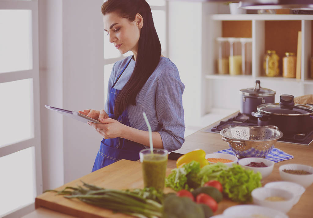 Mujer joven usando una tableta para cocinar en su cocina - Foto, imagen